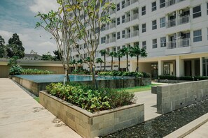 Un bâtiment moderne doté de nombreux balcons, d’une cour aménagée avec un élément décoratif aquatique et d’une grande variété de plantes.