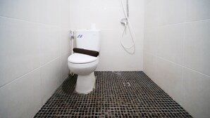 Eine kleine, weiße Toilette mit braunem Sitz und weißem Tank in einem gefliesten Badezimmer mit schwarz-weiß kariertem Boden.