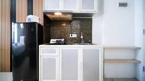 Eine kleine Küche mit weißen Schränken, einem schwarzen Kühlschrank, einer gefliesten Spritzschutzwand und einer Arbeitsplatte.