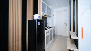 Ein schmaler Flur mit einem schwarzen Kühlschrank, einer weißen Tür und einer kleinen Küchenzeile mit Schränken und einem Spülbecken.