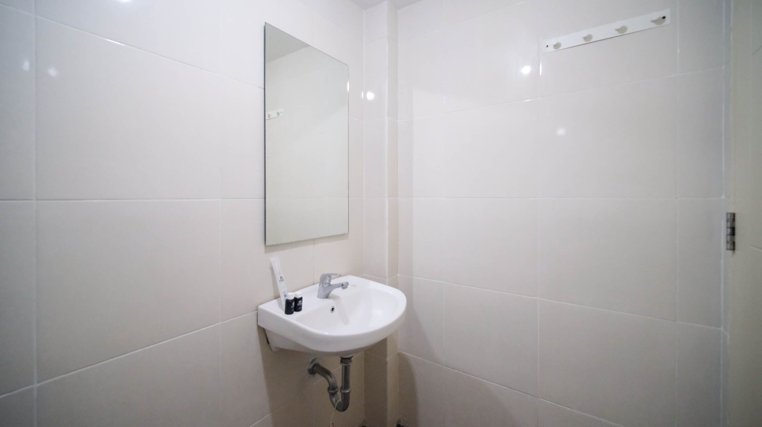 A bathroom with white tiles, a white sink, a mirror, and a towel rack.