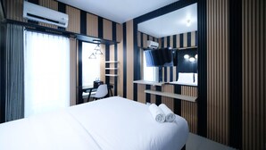 Ein Hotelzimmer mit einem großen Bett, einem Schreibtisch mit Stuhl, einem Fernseher und einer Klimaanlage.