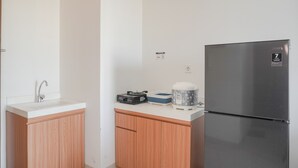 Una cocina con encimera blanca, refrigerador de acero inoxidable, armarios de madera y un lavamanos.