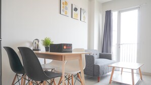 Una sala de estar moderna con una mesa de comedor, dos sillas negras, un sofá gris y una pequeña mesa blanca. Hay tres cuadros enmarcados en la pared y una planta en maceta sobre la mesa.