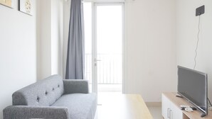 Una sala de estar moderna con un sofá gris, un televisor de pantalla plana sobre un soporte de madera y un ventanal corredizo que da a un balcón.