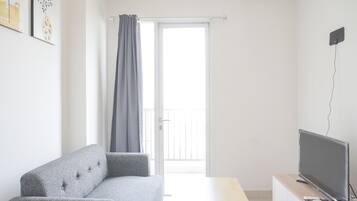 A modern living room with a grey sofa, a flat-screen TV on a wooden stand, and a sliding glass door leading to a balcony.