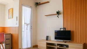 A modern living room with a wooden TV stand, a flat-screen TV, and a sliding glass door. - Spacious And Cozy Studio Tokyo Riverside Pik 2 Apartment (Jakarta)