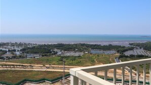 A coastal landscape with a view of the sea, a green area with pathways, and a white railing. - Spacious And Cozy Studio Tokyo Riverside Pik 2 Apartment (Jakarta)