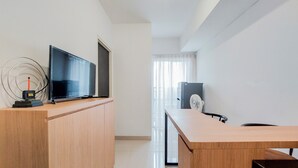 A modern, well-lit room with a wooden desk, a flat-screen TV, and a standing fan.