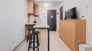 A compact kitchen with a wooden counter, stools, and a TV on a stand.