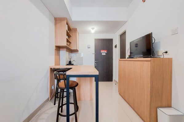 A compact kitchen with a wooden counter, stools, and a TV on a stand.