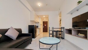 A modern living room with a sofa, a glass coffee table, and a kitchen area with a TV and counter. - Comfortable And Homey Living 2Br At Sky House Bsd Apartment (Pagedangan)