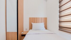 Een klein, net opgemaakt bed met een houten hoofdbord en een wit kussen in een minimalistische kamer met een houten nachtkastje en een klein tafeltje.