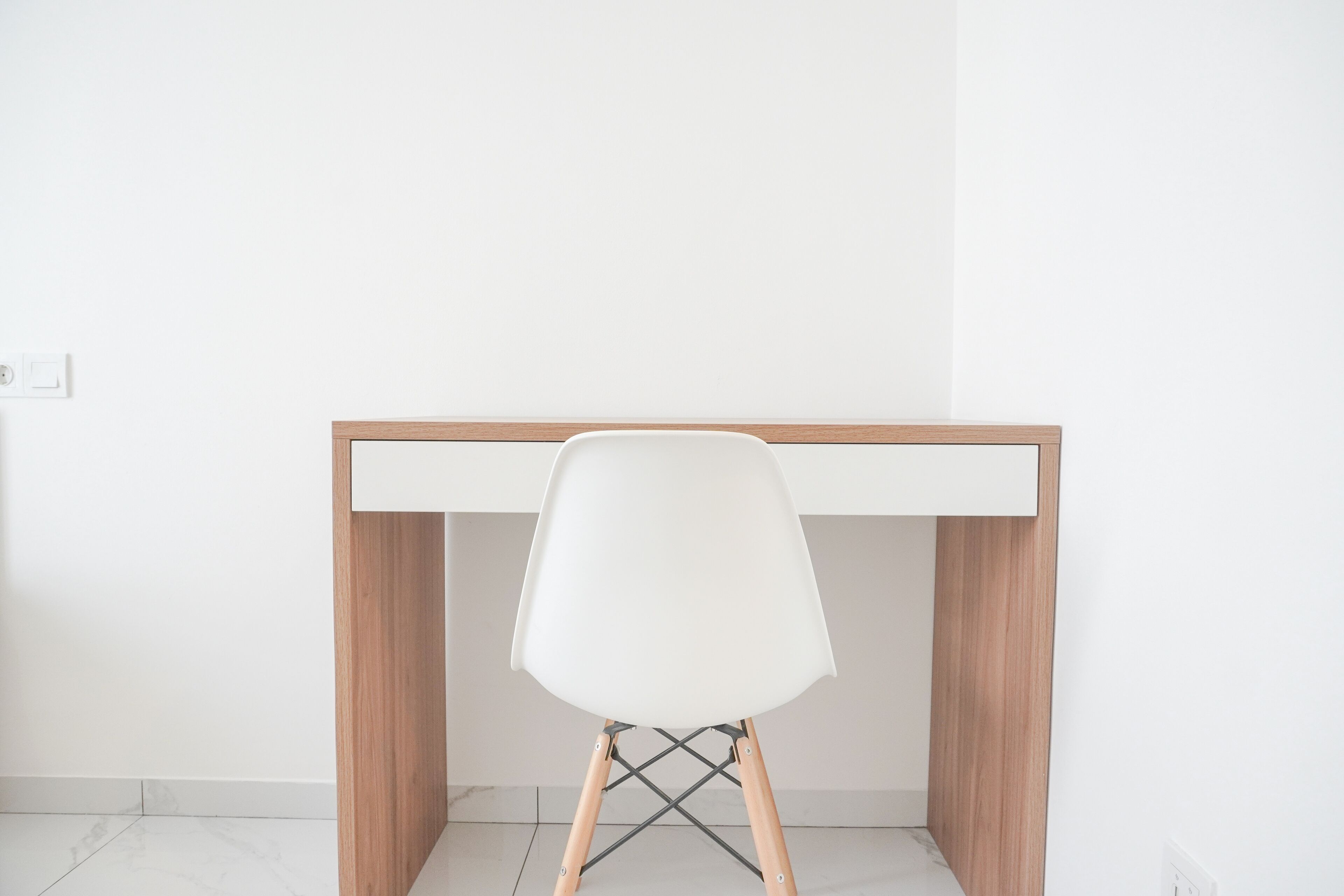 Un escritorio minimalista con una silla blanca en una habitación limpia de paredes blancas.