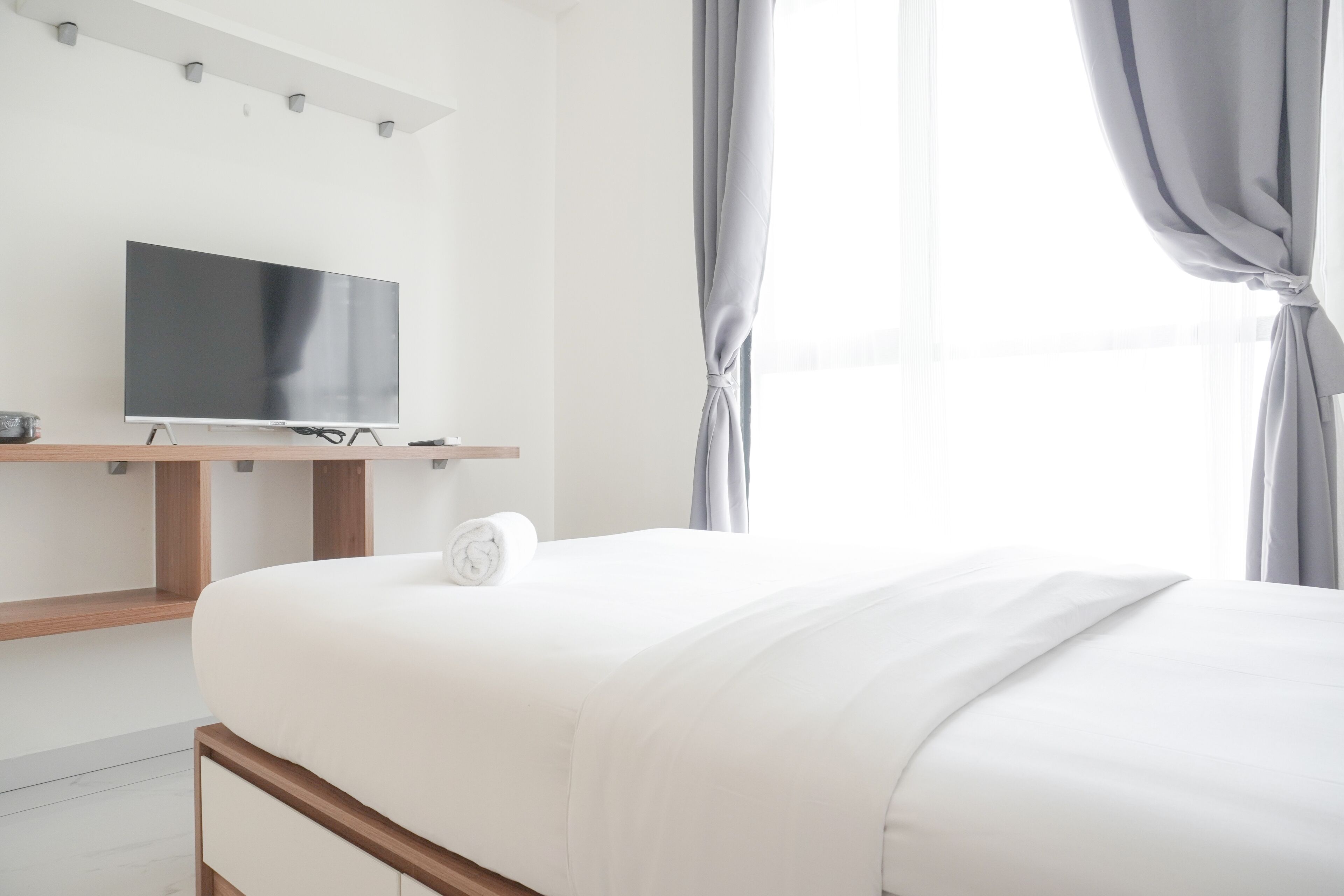 A modern hotel room with a large bed, a flat-screen TV mounted on a wooden stand, and a window with curtains.
