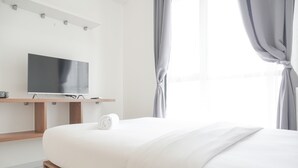 A modern hotel room with a large bed, a flat-screen TV mounted on a wooden stand, and a window with curtains.