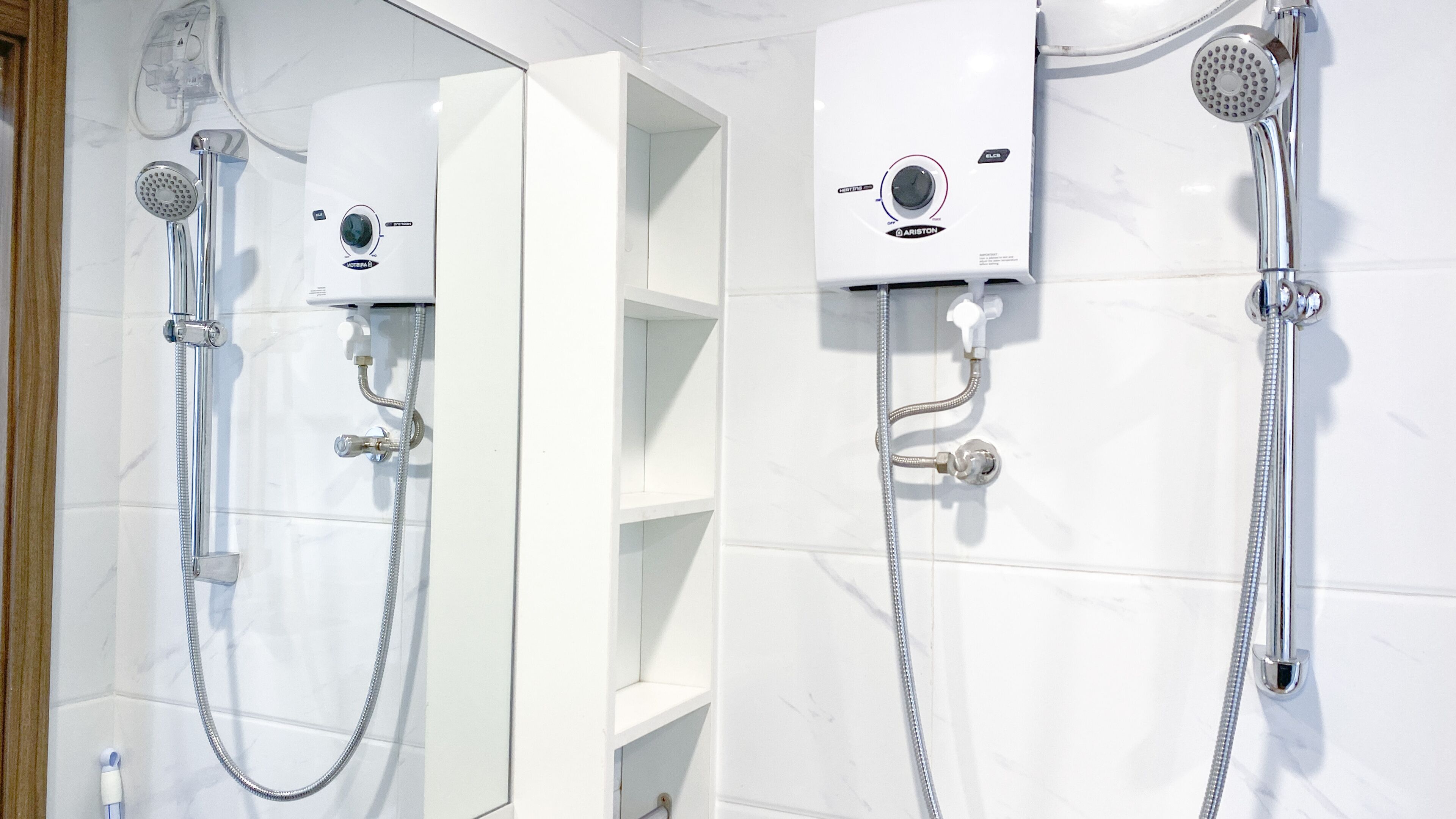 Een badkamer met een witte betegelde muur, een inbouwdouche en een spiegel.