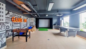 A modern room with a foosball table, a pool table, and a large screen.