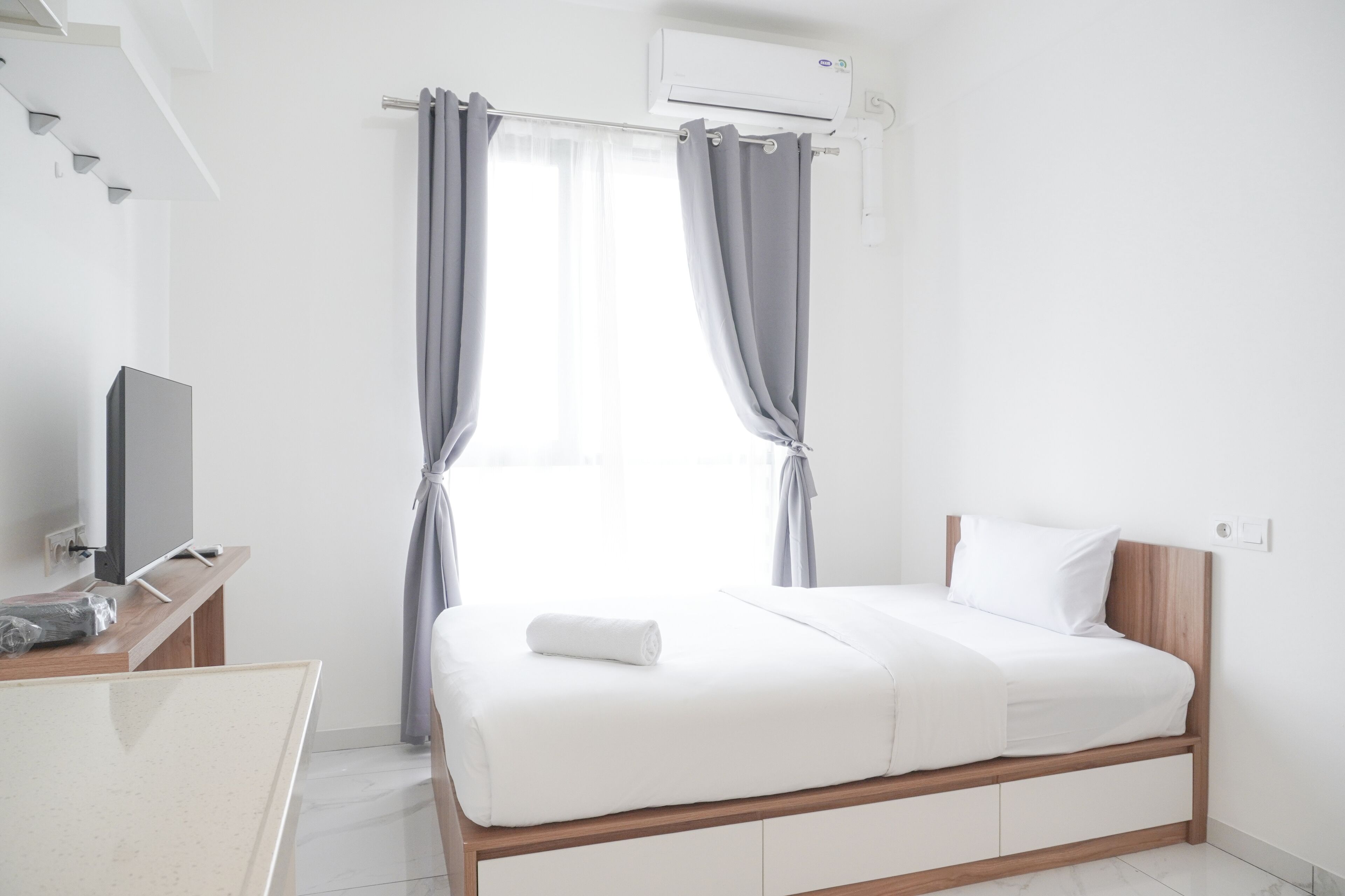 A modern hotel room with a bed, a TV, a desk, and an air conditioning unit.