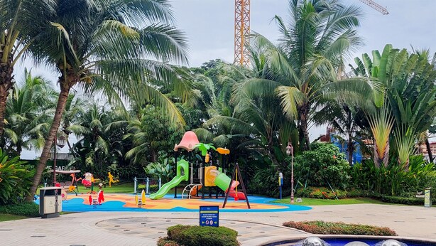 A playground with slides and swings surrounded by palm trees and a water feature.