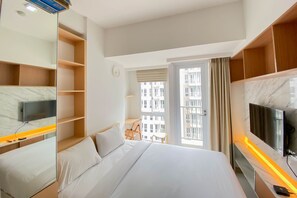 A hotel room with a bed, a TV mounted on the wall, a desk, and a chair. - Nice And Compact Studio At Tokyo Riverside Pik 2 Apartment (Teluknaga)