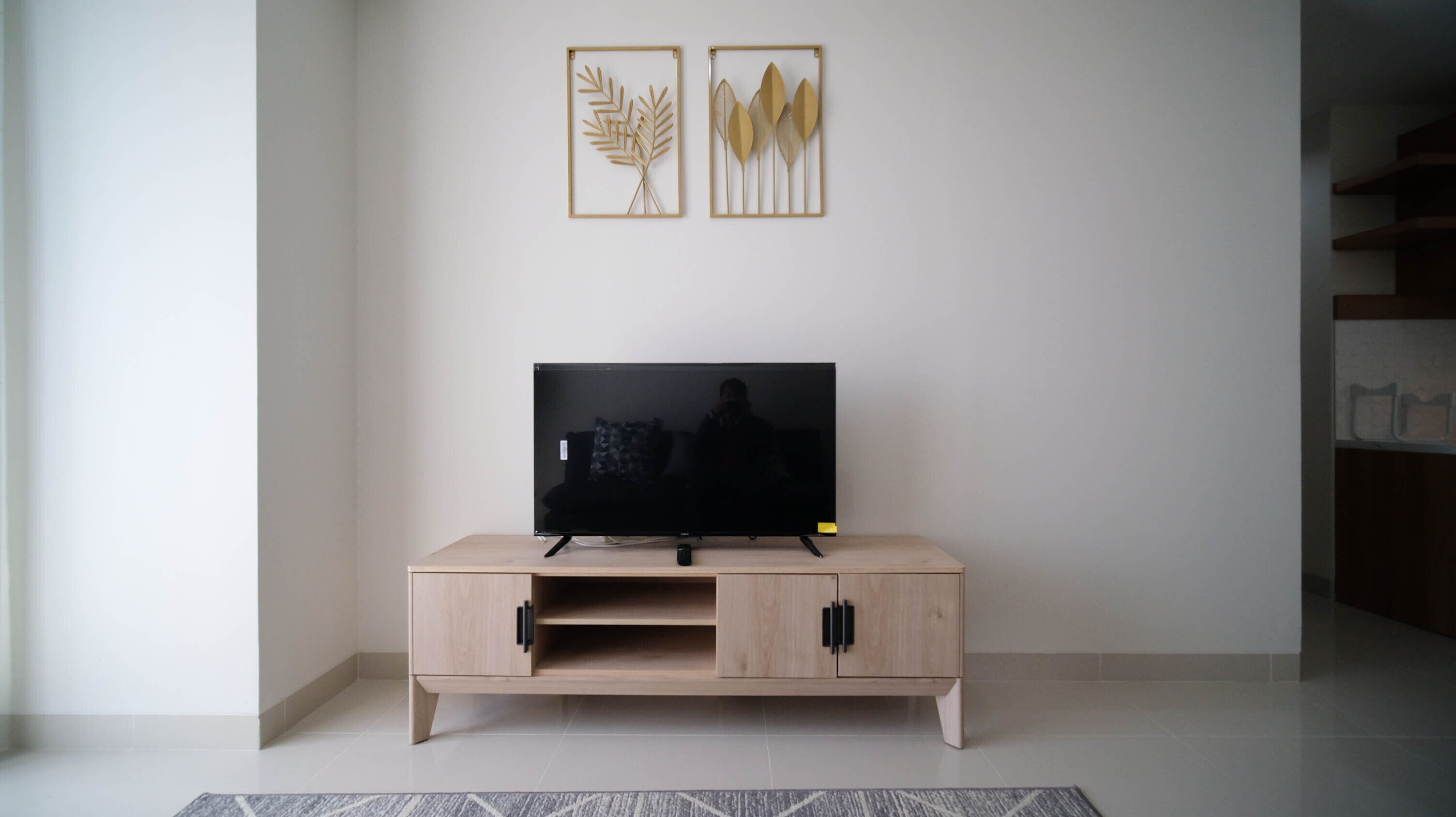 A modern living room with a flat-screen TV on a wooden TV stand, a small cabinet, and two framed wall art pieces above the TV.