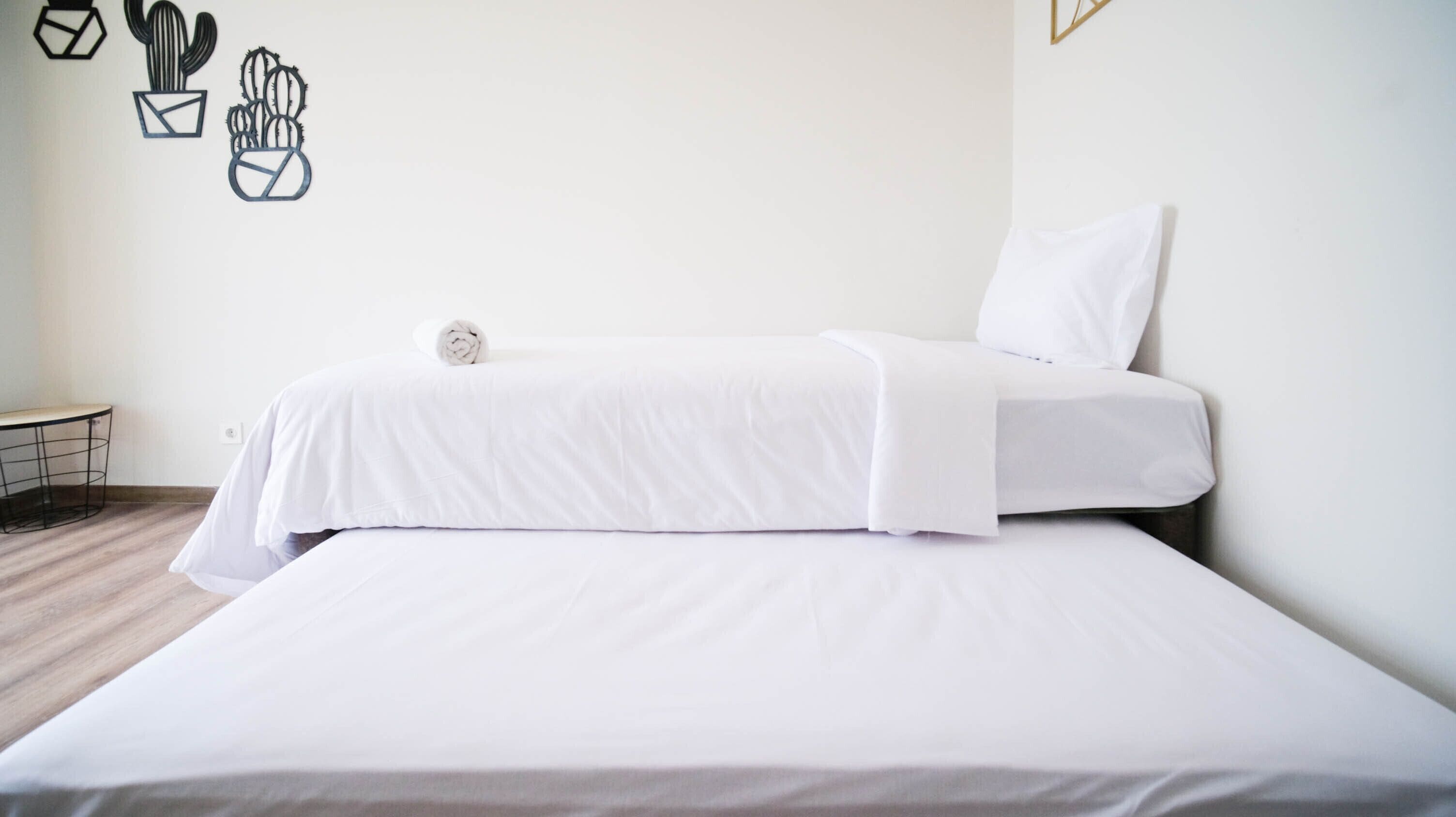 Une chambre d’hôtel au style minimaliste, avec un grand lit, une petite table ronde et un mur décoré de motifs géométriques représentant des cactus.