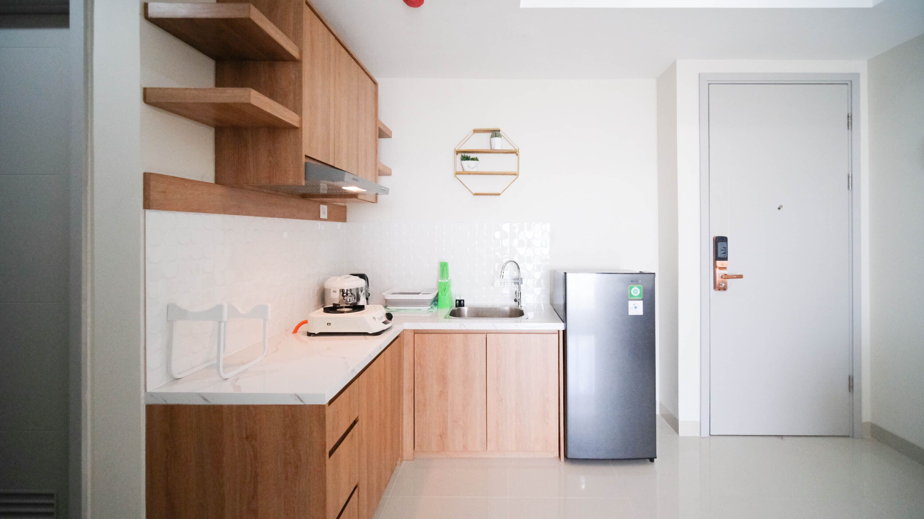 A modern kitchen with wooden cabinets, a stainless steel refrigerator, a coffee maker, and a small shelf with plants.