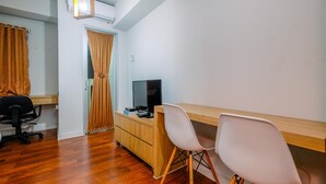 A room with a wooden desk, two white chairs, a television, and a wardrobe. - Simply Look Studio (No Kitchen) At Dramaga Tower Apartment (Dramaga)