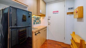 A compact kitchen with wooden cabinets, a black refrigerator, a small countertop, and a wooden bench. - Simply Look Studio (No Kitchen) At Dramaga Tower Apartment (Dramaga)