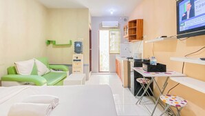 Une chambre d’hôtel comprenant un lit, un canapé vert, une petite table, un téléviseur et un coin cuisine.