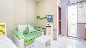 Une petite pièce propre, avec un canapé vert et blanc, une table blanche, un distributeur d’eau et une porte-fenêtre coulissante sur le côté droit.