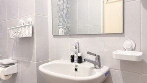 Une salle de bain avec un lavabo blanc, un miroir et une étagère contenant des articles de toilette.