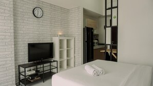 Ein Hotelzimmer mit Backsteinwand, einem Flachbildfernseher, einem Bett mit weißer Bettwäsche und einer Holztür zu einer Küchenzeile.