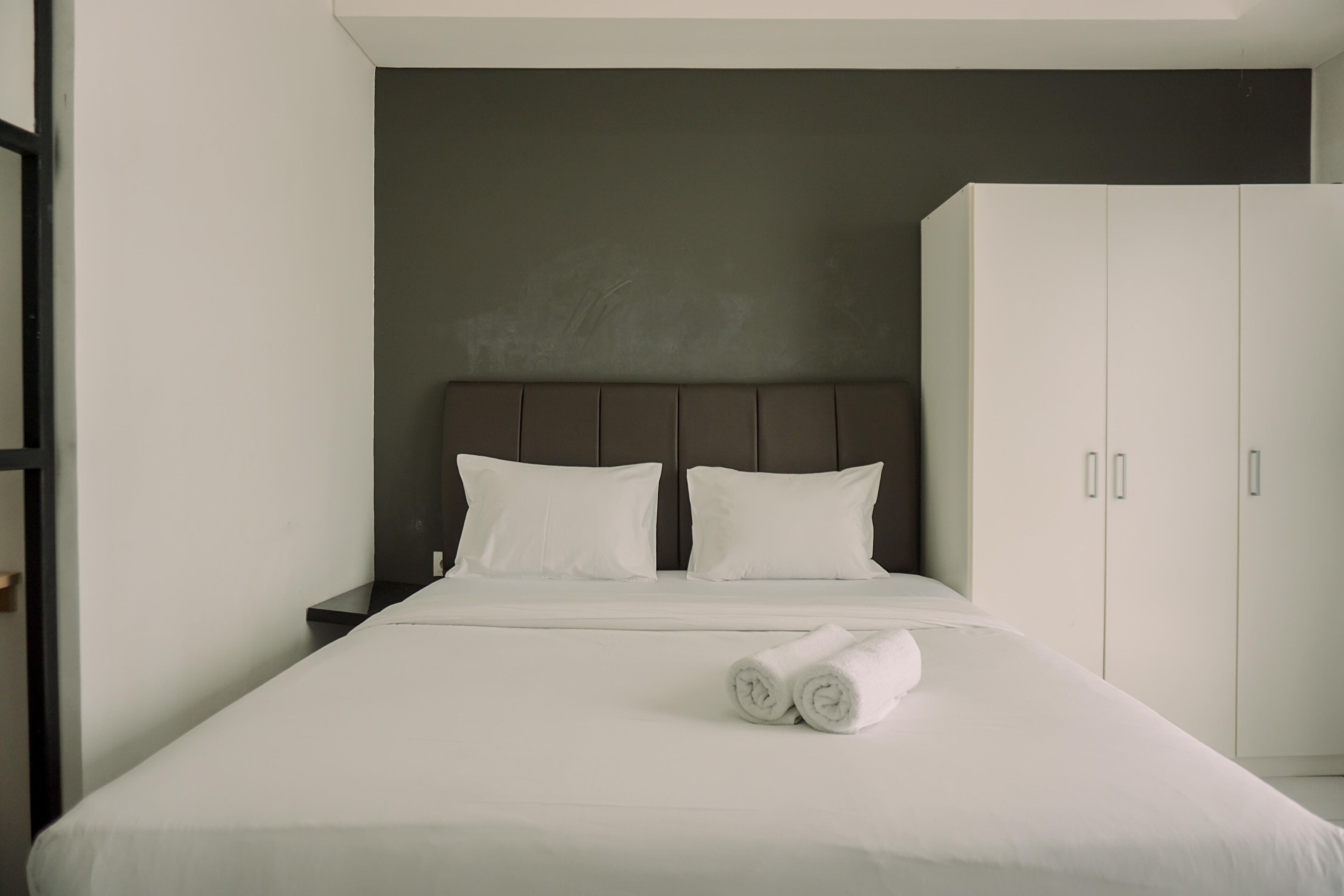 A modern hotel room with a large bed, two pillows, a nightstand, and a wardrobe.