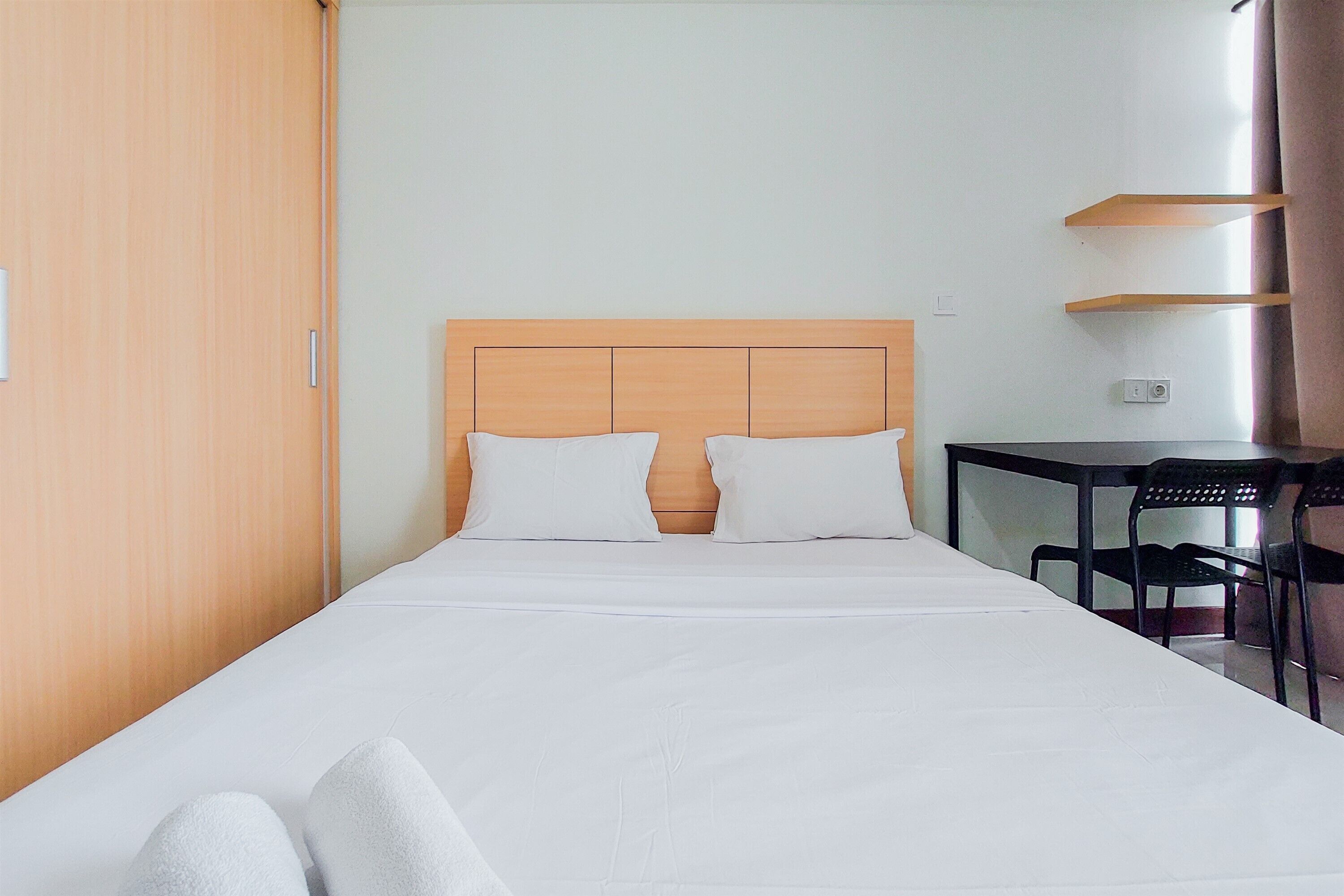 A hotel room with a wooden headboard, white bedding, a small table with chairs, and a wooden wardrobe.