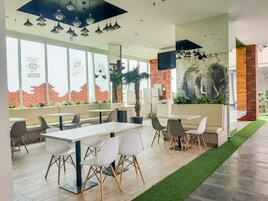 A modern restaurant with white tables and chairs, large windows, and a mural of an elephant.