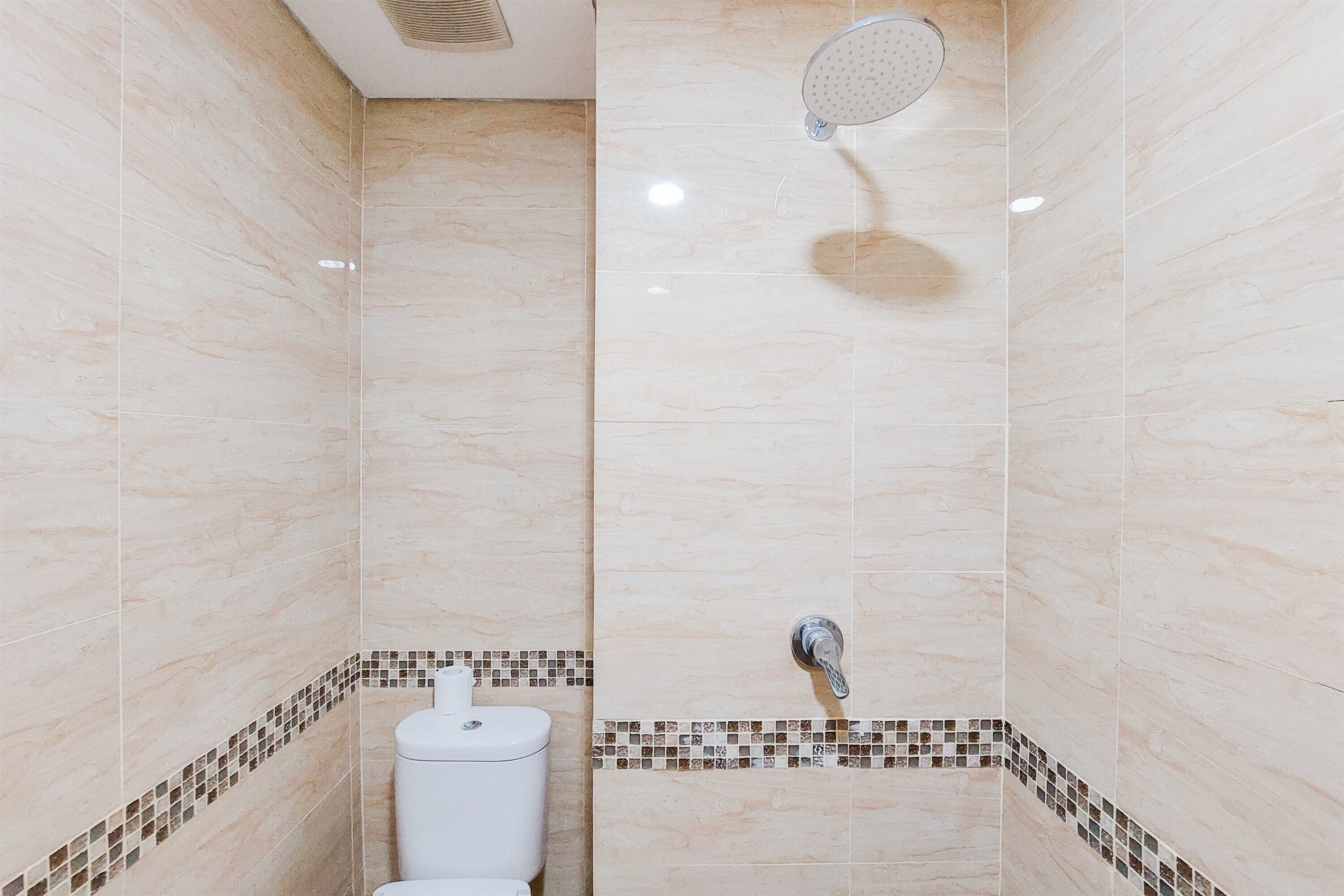 Un baño pequeño y azulejado con ducha, inodoro y un diseño de azulejos en esquina.