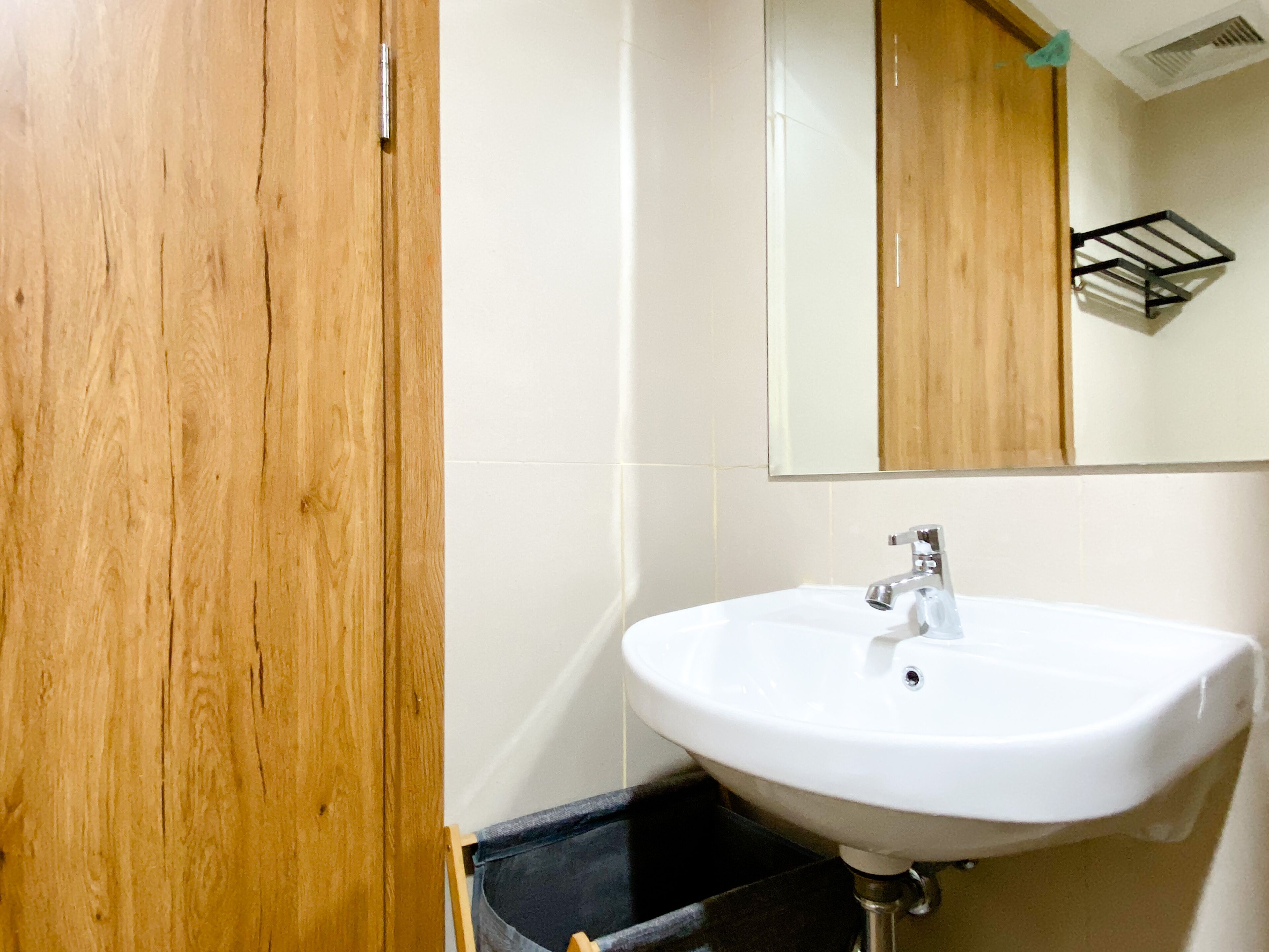 A bathroom with a wooden door, white tiles, a white sink, and a mirror.