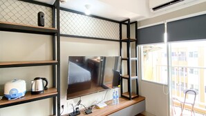 A modern room with a large flat-screen TV mounted on a black metal shelf, a coffee maker, a kettle, and a water dispenser on the counter. - Homey and Simply Look Studio LRT City Jatibening Apartment (Bekasi)