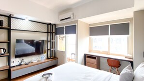 A hotel room with a bed, a desk with a chair, a TV, and a window with blinds. - Homey and Simply Look Studio LRT City Jatibening Apartment (Bekasi)