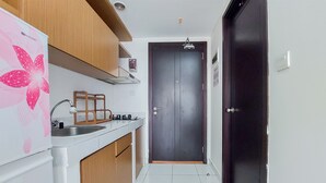 A narrow kitchen with white cabinets, a stainless steel sink, and a dark wooden door. - Warm And Enjoy Living Studio Casa De Parco Apartment (South Tangerang)