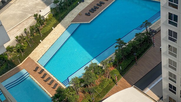 A large rectangular swimming pool with a wooden deck area and lounge chairs. - Simply Look Studio Tokyo Riverside Pik 2 Apartment (Teluknaga)