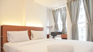 A hotel room with a wooden headboard, white bedding, a desk with a telephone, and curtains on the windows. - Simply Look Studio Tokyo Riverside Pik 2 Apartment (Teluknaga)