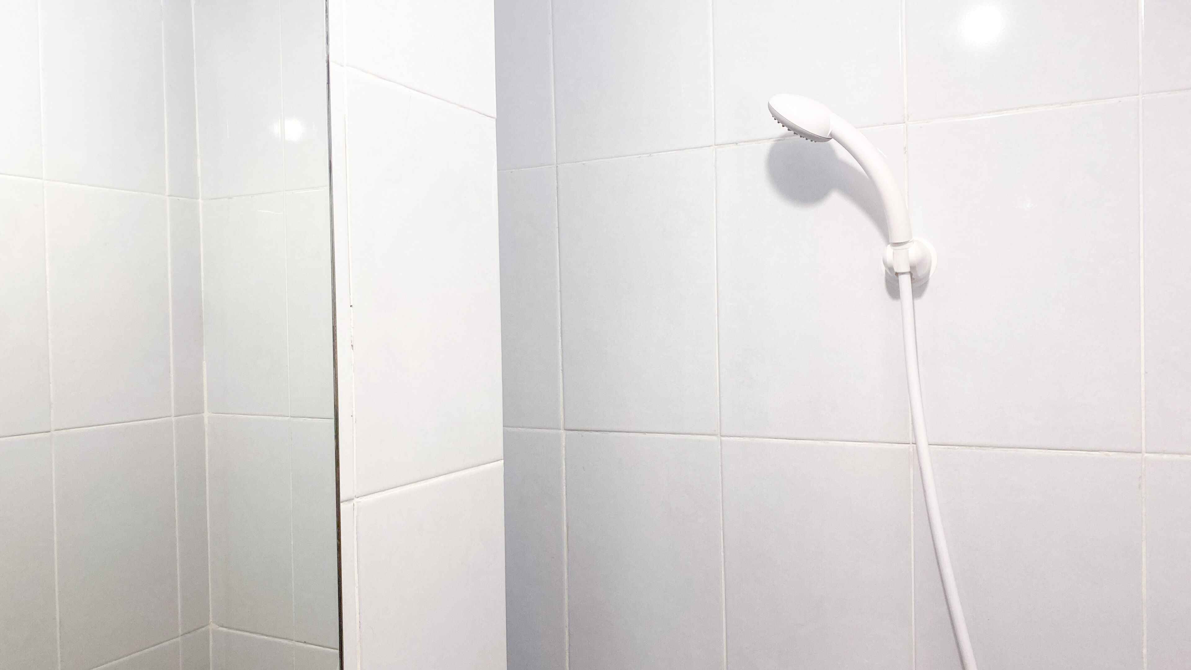 Un espacio de ducha con azulejos blancos y un cabezal de ducha manual.