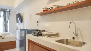 A modern kitchen with white tiles, a stainless steel sink, wooden cabinets, and a built-in TV. - Simply Look Studio Tokyo Riverside Pik 2 Apartment (Teluknaga)