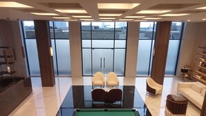 A modern indoor pool area with a pool table, two white chairs, a sofa, and a small round table. - Exclusive And Homey 3Br Loft At Kingland Avenue Apartment (South Tangerang)