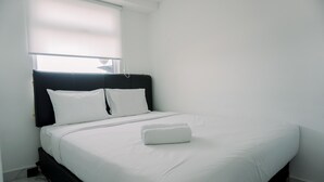A neatly made bed with white linens and a folded towel in a clean, white room with a black headboard. - Exclusive And Homey 3Br Loft At Kingland Avenue Apartment (South Tangerang)