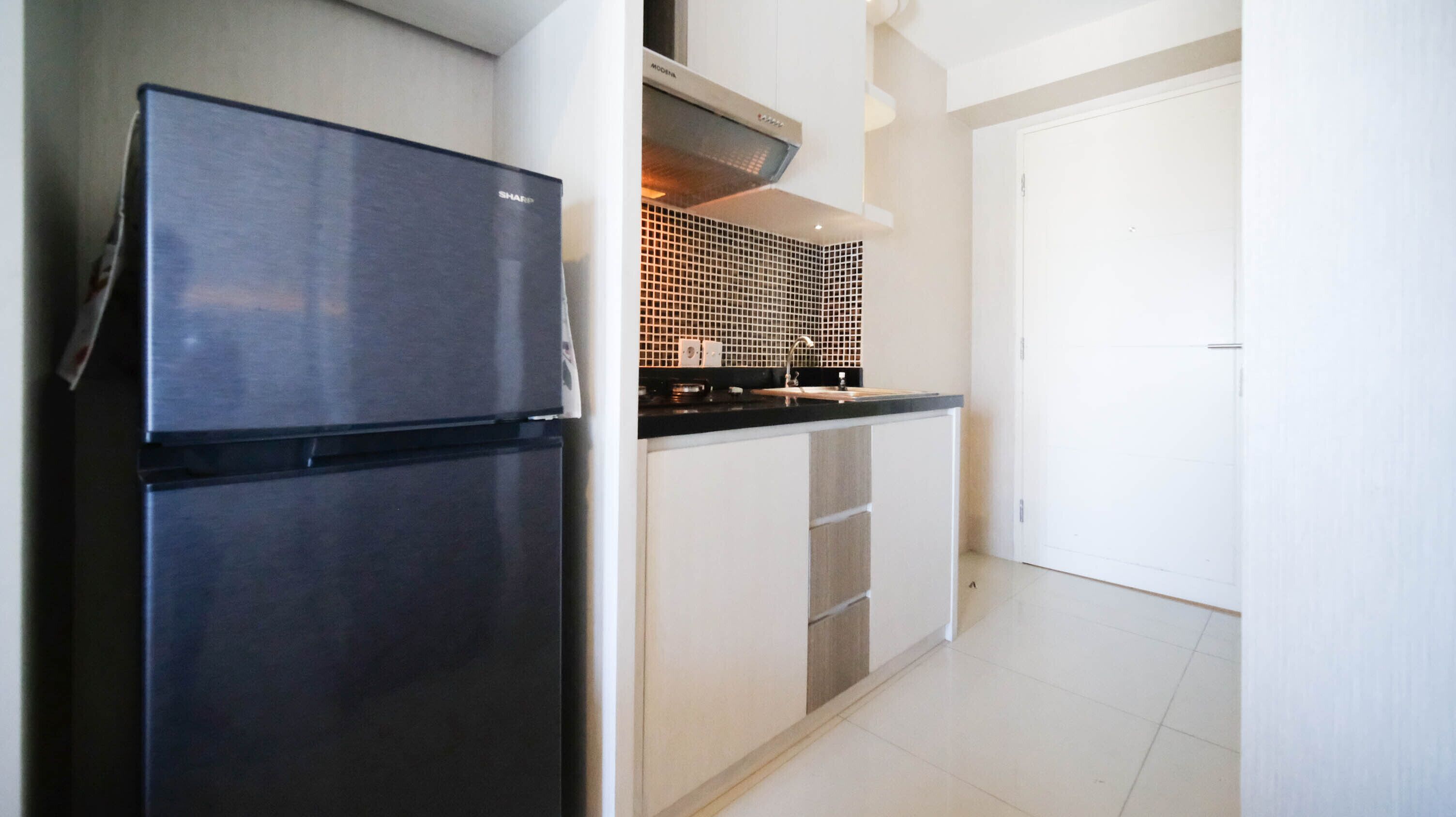 A compact kitchen with a double refrigerator, a tiled backsplash, and a white door.