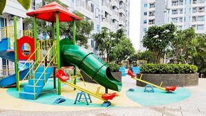 A playground with a green slide, red and yellow swings, and a red climbing structure. - Nice Studio Connected To Mall At Tanglin Supermall Mansion Apartment (Surabaya)